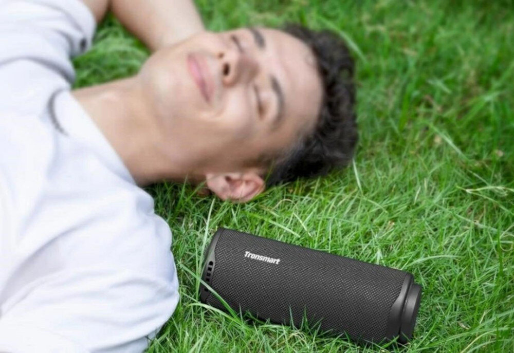 Głośnik TRONSMART T8 ultralekki z odpinanym paskiem do przenoszenia, Mężczyzna leżący na trawie, obok niego głośnik T8