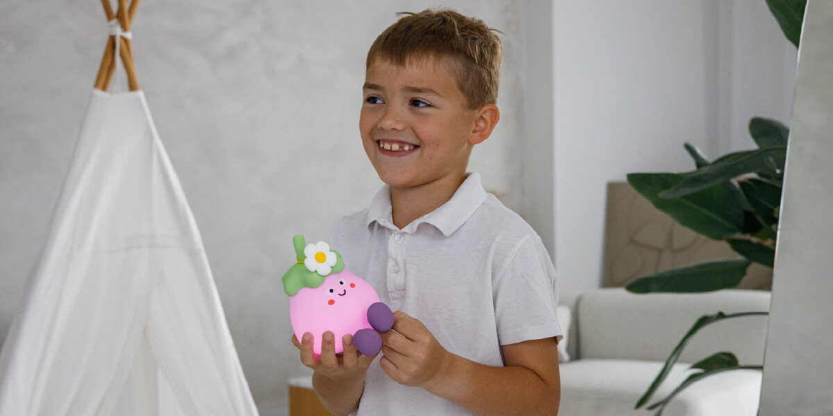 Lampka nocna INNOGIO GIOegplant Bakłażan GIO-147, światło, przyjazne, regulowanie, dotyk, dziecko trzyma lampkę w rękach i się uśmiecha