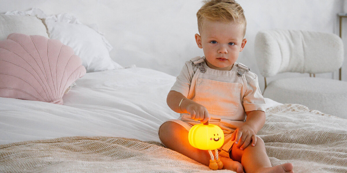 Lampka nocna INNOGIO GIOpumpkin Dynia GIO-146, silikon, dotyk, bezpieczna, elastyczna, dziecko siedzi na łóżku i trzyma w ręku lampkę