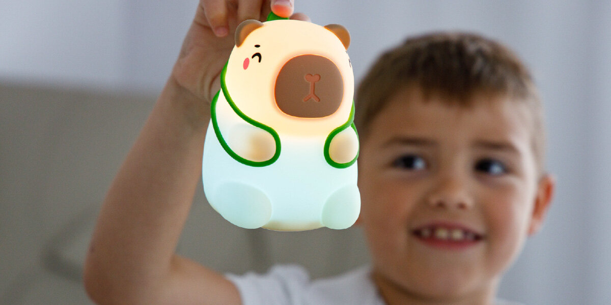 Lampka nocna INNOGIO GIOcapybara Kapibara GIO-154, ciepłe, światło, kolorowe, klimat, dziecko trzyma w ręce lampkę kapibara i spogląda na nią