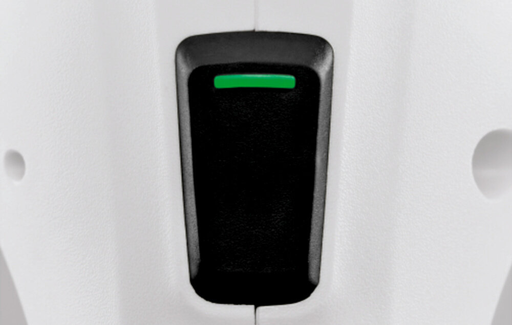 Zbliżenie na czarny przycisk z zielonym paskiem na białej powierzchni urządzenia.