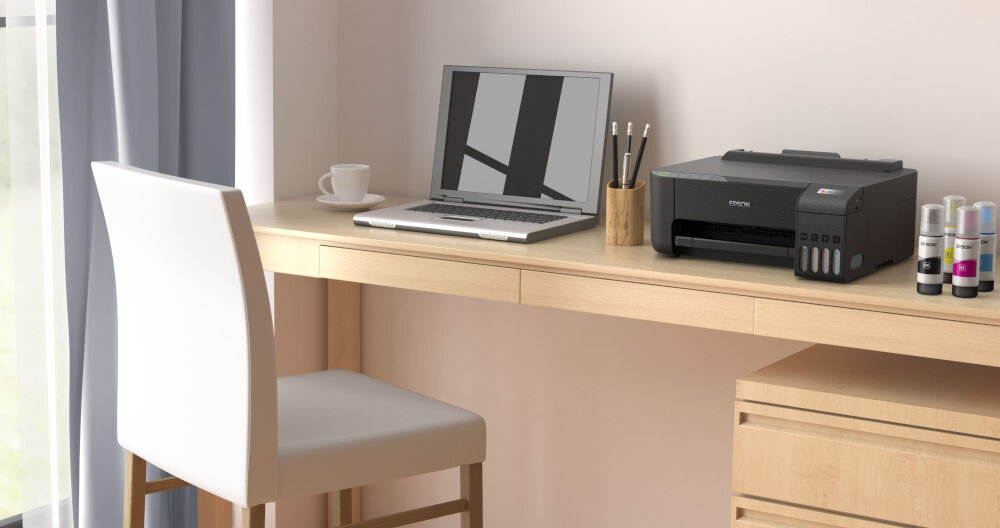 Drukarka EPSON EcoTank L1270 Wi-Fi prezentacja drukarki w jasnym pokoju na biurku laptop butelki z atramentem filiżanka i ołówki obok z systemem stałego zasilania w atrament