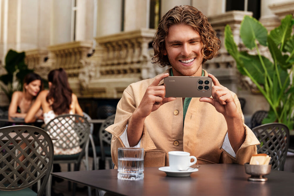 Smartfon XIAOMI 15T Pro 5G 12/1TB 6.83 cali 144Hz Złoty mężczyzna trzymający smartfon w dłoniach siedzący w restauracji na dworze przekątna smukłe ramki jasność rozdzielczość odświeżanie DC dimming Flicker-Free