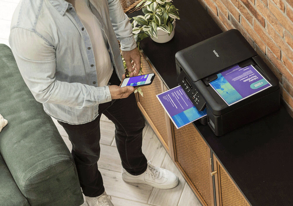 Urządzenie wielofunkcyjne BROTHER DCP-T735DW Druk w kolorze, Automatyczny druk dwustronny, Wi-Fi mężczyzna stojący przy urządzeniu i trzymający telefon w dłoni z włączoną aplikacją w pomieszczeniu rozdzielczość skanowania w kolorze dokumenty zdjęcia rozdzielczość interpolowana wysoka jakość