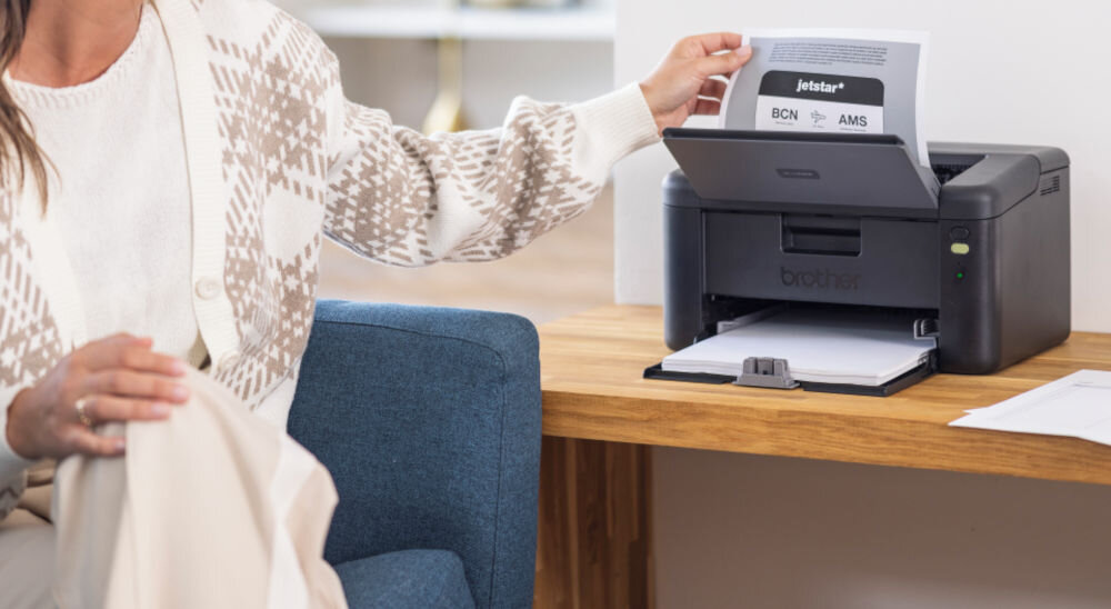 Drukarka BROTHER HL-L1232W, Wi-Fi prezentacja urządzenia podczas korzystania kobieta wyciągająca kartkę z drukarki prędkość druku tryb monochromatyczny eliminacja długiego czasu oszekiwania czas potrzebny na wydruk pierwszej strony