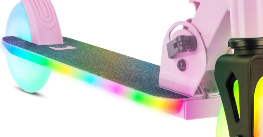 Fragment różowej hulajnogi z widocznym podestem pokrytym ciemnym materiałem antypoślizgowym i świecącymi krawędziami w różnych kolorach. Koło hulajnogi jest półprzezroczyste i również emituje kolorowe światło.