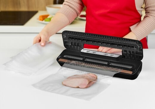Pakowanie plasterków mięsa do woreczka próżniowego przy użyciu zgrzewarki  MPZ-02. Otwarta zgrzewarka na kuchennym blacie.