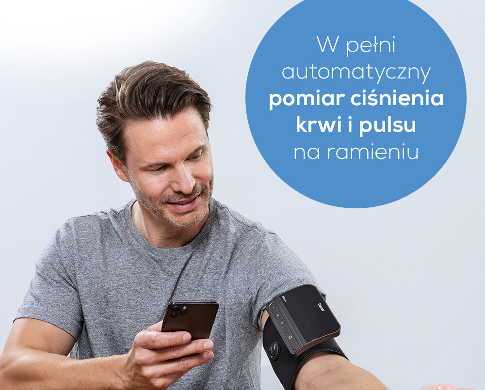 Osoba używa ciśnieniomierza na ramieniu, trzymając w ręku smartfon. Na obrazie widoczny jest tekst: \'W pełni automatyczny pomiar ciśnienia krwi i pulsu na ramieniu\'.