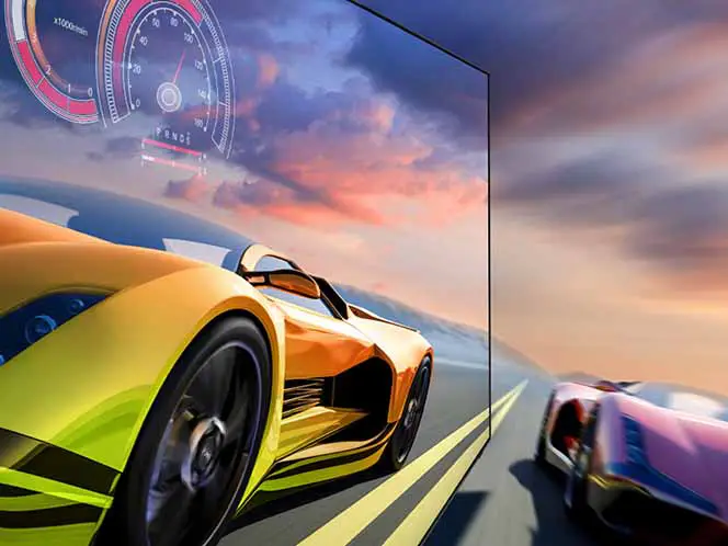Obraz przedstawia dwa sportowe samochody w ruchu na tle zachodzącego słońca, widoczne na ekranie telewizora. W lewym górnym rogu ekranu znajduje się graficzny wskaźnik prędkościomierza.
