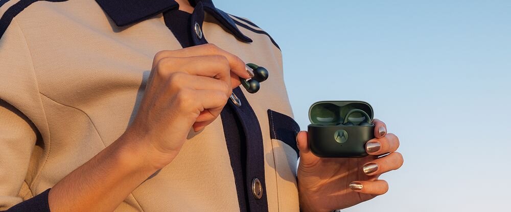 Motorola Moto Buds Loop przetworniki 12 mm ironless czysty dźwięk bogate tony, osoba trzymająca słuchawki wraz z etui ładującym w rękach