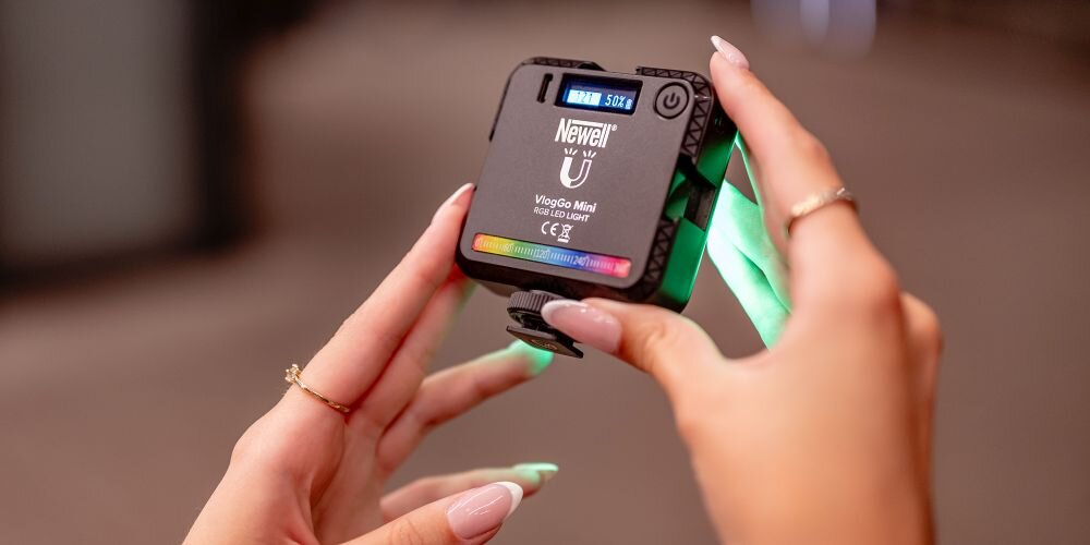 Osoba trzyma urządzenie z napisem \'Newell VlogGo Mini RGB LED\'. Urządzenie emituje zielone światło z boku.