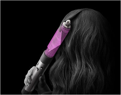Osoba używa suszarko-lokówki z różową końcówką na włosach. Tło jest ciemne, a urządzenie ma metaliczny korpus.