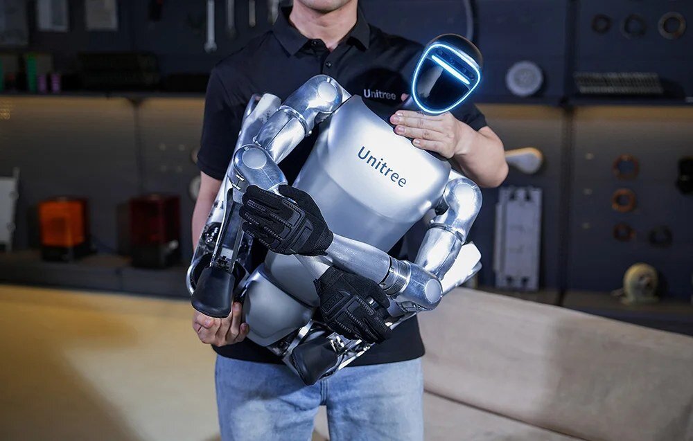 Mężczyzna trzyma na rękach kompaktowo złożonego robota humanoidalnego Unitree G1 z podświetlaną głową.