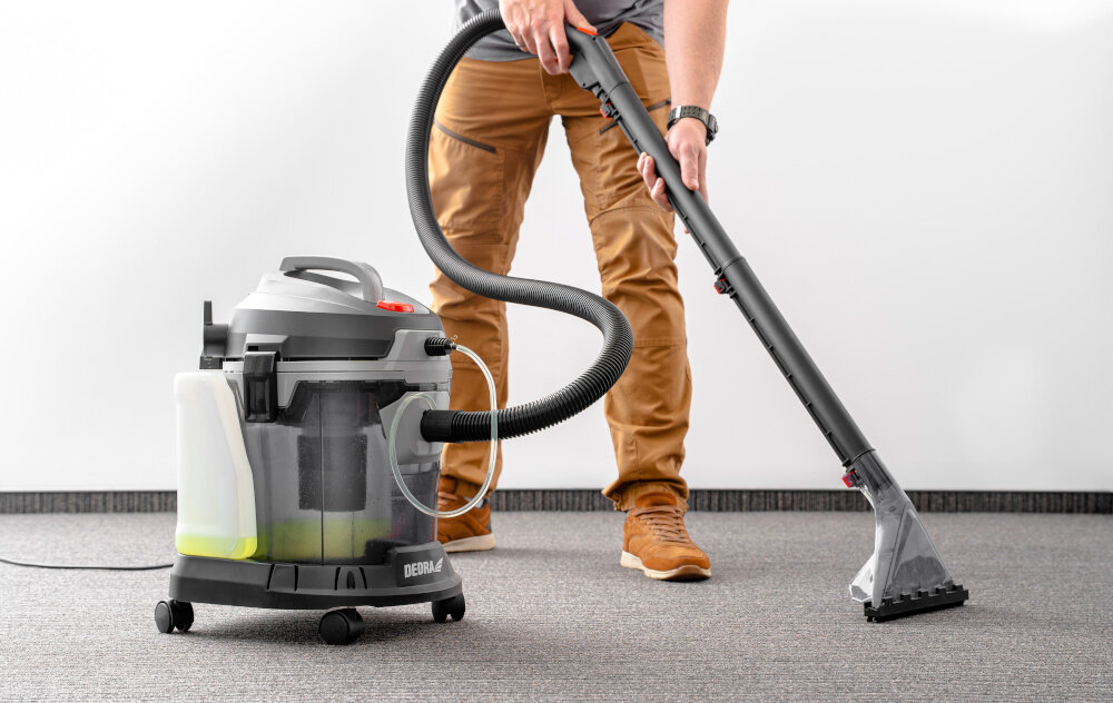 Odkurzacz piorący DEDRA DED6608 pomieszczenie osoba odkurza dywan w tle biała ściana wszechstronne czyszczenie odkurzanie pranie