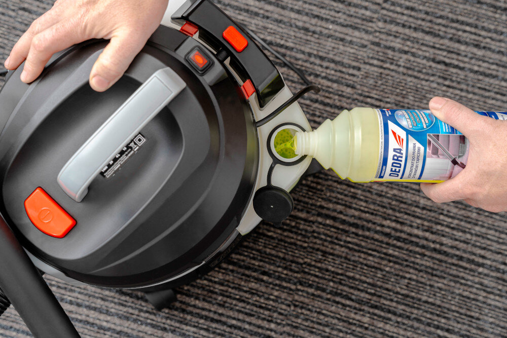 Odkurzacz piorący DEDRA DED6608 pomieszczenie odkurzacz stoi na dywanie osoba uzupełnia zbiornik środkiem czyszczącym zbiornik główny o pojemności 15 litrów zbiornik na wodę z detergentem o pojemności 4 litry czyszczenia na mokro przeźroczysty materiał zbiornika