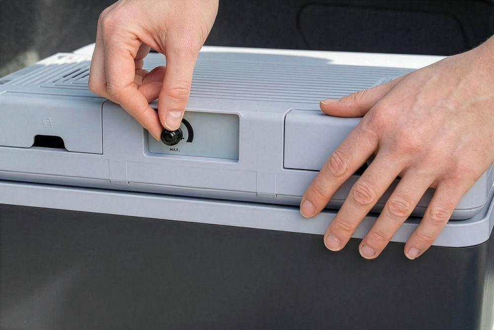 Lodówka turystyczna GÖTZE & JENSEN TC810G Zbliżenie na dłoń regulującą temperaturę za pomocą czarnego pokrętła na górnej pokrywie lodówki turystycznej.