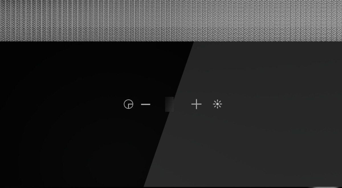 OKAP AKPO WK-9 CLARA CZARNY T500 Zdjęcie ukazuje fragment panelu sterowania okapu z ikonami regulacji mocy i oświetlenia, umieszczonymi na połyskującej czarnej powierzchni. Nad panelem znajduje się metalowy filtr o gęstej strukturze wydajna turbina cicha praca pilot timer sterowanie