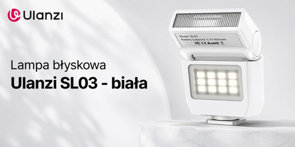 Lampa błyskowa w kolorze białym ustawiona na podwyższeniu, widoczna regulowana głowica i panel LED oraz logo producenta