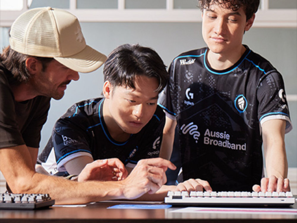 LOGITECH G Pro X Superlight 2C bezprzewodowa forma konstrukcja zawodnikami e-sportu - Trzech graczy w czarnych koszulkach esportowych podczas wspólnej gry i dyskusji przy klawiaturach.