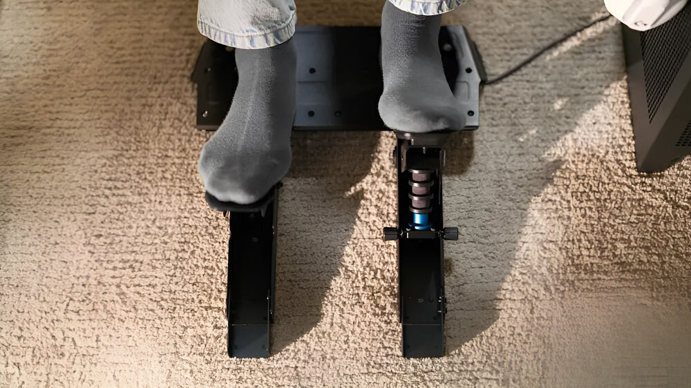 Zestaw pedałów gaz + hamulec LOGITECH RS 941-000310 pokazanie wciskania pedałów nogi na nich konstrukcja na jasnym dywanie stalowa platforma z przedłużkami bez przechylania