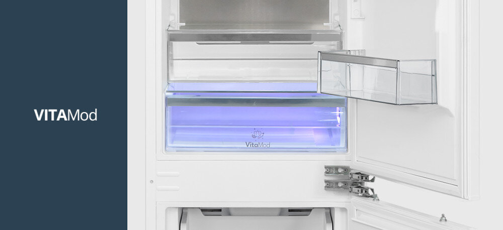 Lodówka VESTFROST VR-BB27633H0DD Na zdjęciu widoczna jest dolna część komory chłodziarki z podświetlaną na kolor fioletowo-niebieski szufladą VitaMod. Po lewej stronie kadru znajduje się granatowy pas z napisem VITAMod Szuflada z kontrolowanym mikroklimatem wydłuża świeżość owoców i warzyw