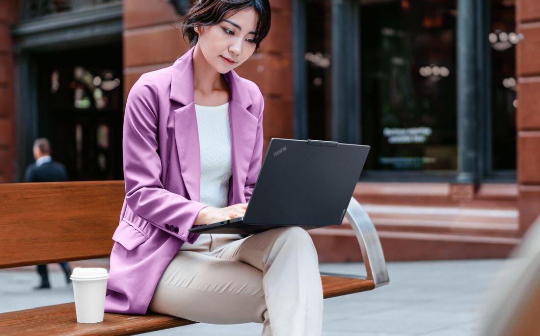 Osoba pracuje na lekkim laptopie Lenovo ThinkPad siedząc na ławce przed budynkiem w przestrzeni miejskiej - WAGA I MOBILNOŚĆ   