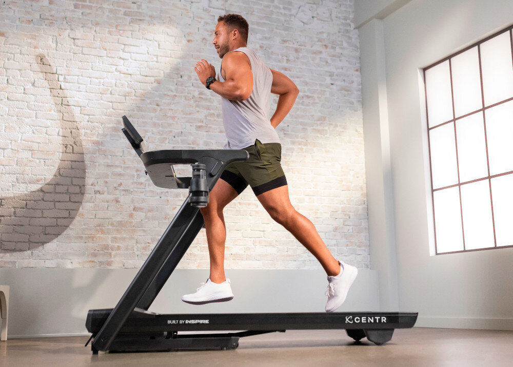 Bieżnia elektryczna CENTR RunR-S 2238W 16km-h pomieszczenie bieżnia na środku pomieszczenia osoba biegnie na bieżni w tle okno ściana z cegły trening w domu zdrowie bieganie chodzenie maszerowanie