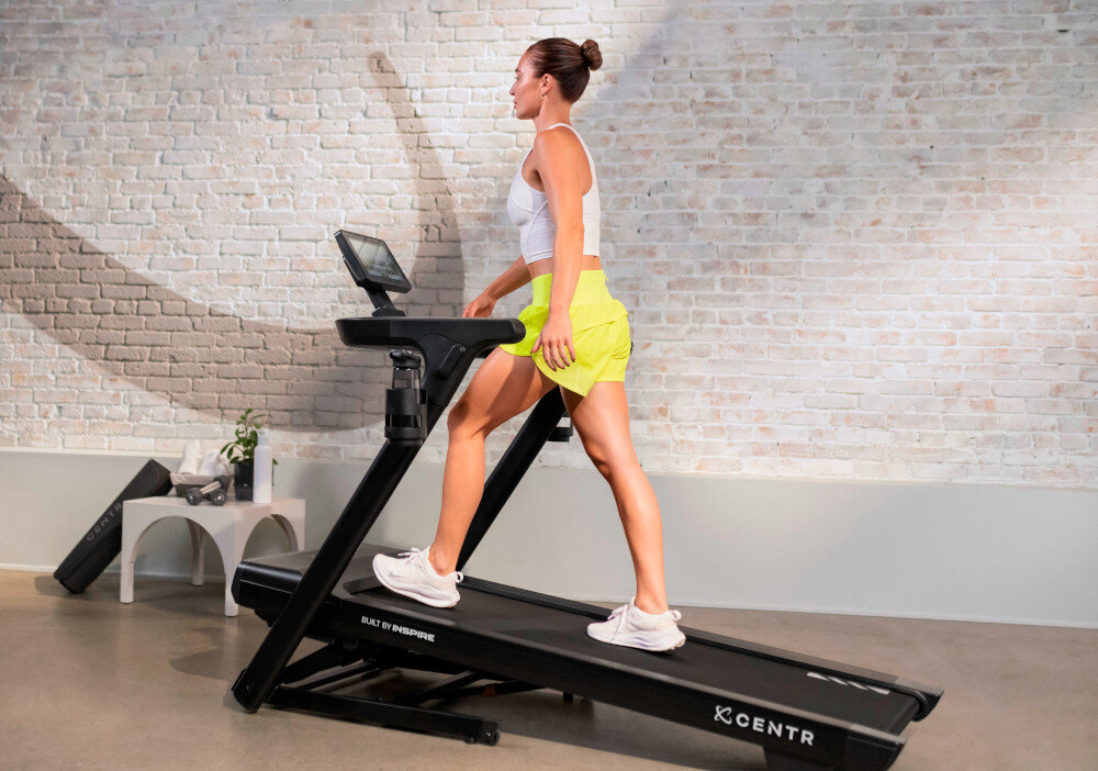 Bieżnia elektryczna CENTR RunR-S 2238W 16km-h pomieszczenie bieżnia na środku pomieszczenia osoba biegnie na bieżni w tle okno ściana z cegły do użytku domowego wspiera utrzymanie dobrej kondycji pomaga w kontrolowaniu masy ciała do marszu truchtu biegania uniwersalne rozwiązanie składana konstrukcja system amortyzacji Cloud Cushion™ wygodna bezpieczna zróżnicowane programy treningowe