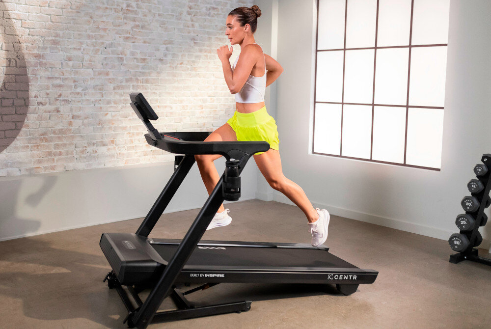 Bieżnia elektryczna CENTR RunR-S 2238W 16km-h pomieszczenie bieżnia na środku pomieszczenia osoba biegnie na bieżni w tle okno ściana z cegły system Cloud Cushion™ amortyzuje wstrząsy zmniejszając obciążenie stawów i kręgosłupa trening jest mniej męczący redukcja wstrząsów do codziennych ćwiczeń intensywnych sesji interwałowych