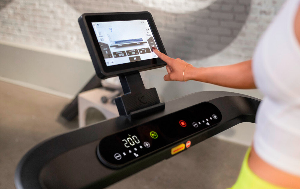 Bieżnia elektryczna CENTR RunR-S 2238W 16km-hb pomieszczenie osoba dotyka ekranu na bieżni w tle ściana z cegły Wi-Fi Bluetooth i zintegrowane głośniki współpracuje z czujnikami tętna Bluetooth bezpieczeństwo efektywne planowanie treningów współpracuje z aplikacjami YouTube Netflix Spotify