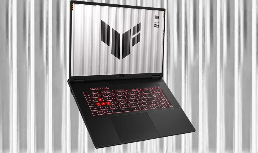 Laptop ASUS TUF Gaming z czerwonym podświetleniem klawiatury stoi przed jasnym, metalicznym tłem przypominającym kontener – Design Aluminiowa pokrywa z subtelnym logo TUF Gaming 