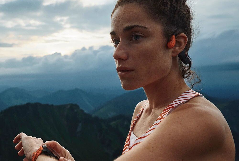 Słuchawki SUUNTO Wing 2 aplikacja Suunto personalizacja audio tryby LED komunikaty głosowe tempo dystans, osoba z założonymi słuchawkami kostnymi