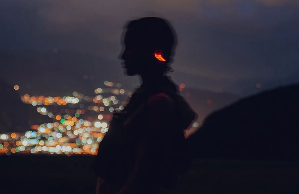 Słuchawki SUUNTO Wing 2 inteligentne diody LED pulsujące z kadencją biegu zwiększające widoczność po zmroku, osoba z założonymi słuchawkami kostnymi, słuchawki z diodami LED