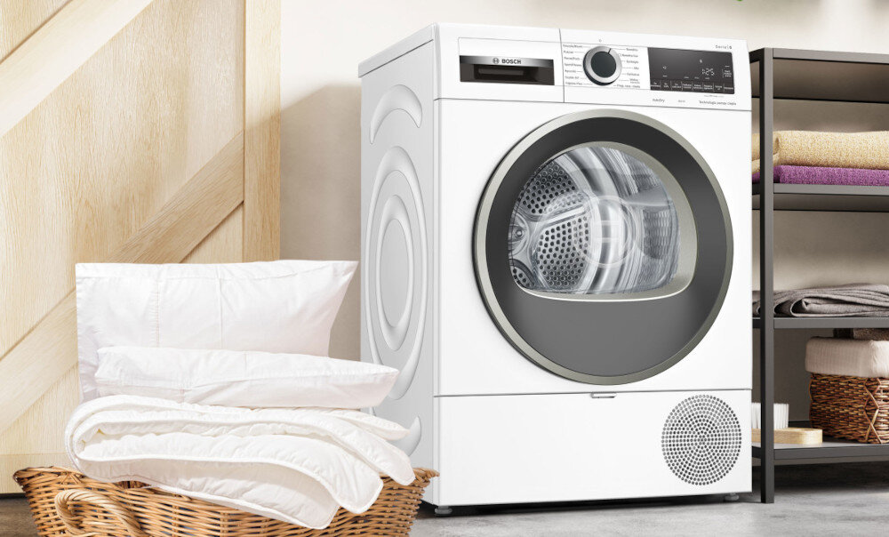 SUSZARKA BOSCH WQG243MSPL Na zdjęciu jest suszarka, a przed nią wiklinowy kosz z białą pościelą. Pomieszczenie wygląda na jasne i uporządkowane program pościel suszenie pościeli równomierne suszenie zapobieganie splątywaniu tkanin suszenie dużych i małych elementów rezultaty suszenia