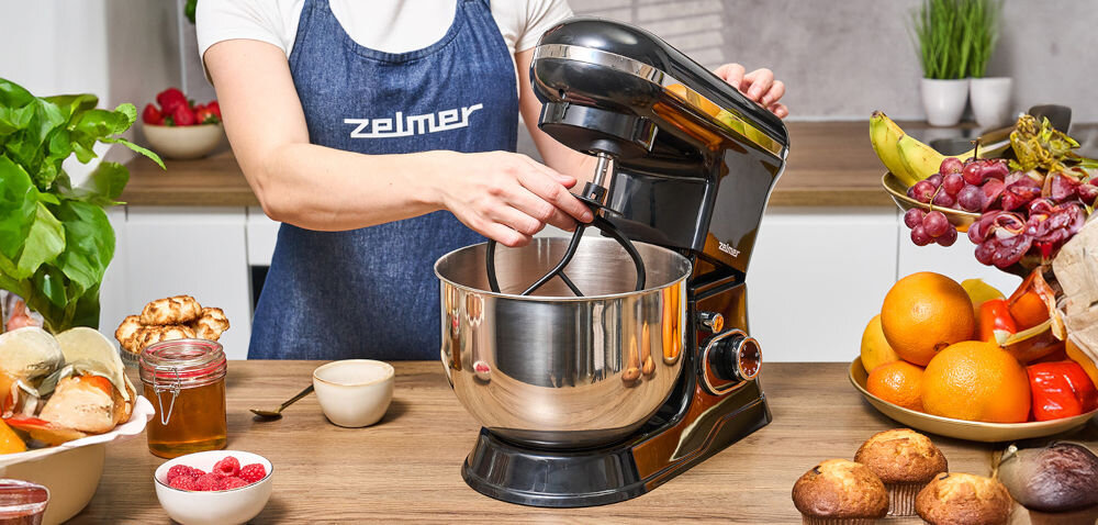 Robot planetarny ZELMER ZKR1355 1200W kuchenne tło robot stoi na blacie czarny kolor srebrna misa pokrętło srebrne elementy ręka zakłada czarną końcówkę wokół robota znajdują się owoce potrawy słodkości moc 1200 W do każdego rodzaju ciasta 6-stopniowa regulacja mocy intuicyjne pokrętło dostosowanie prędkości mieszania funkcja SMART MIX dobiera tempo do gęstości masy PULSE kompaktowe wymiary (41,5 × 24 × 34 cm) przewód o długości 0,98 m swoboda ustawienie na blacie