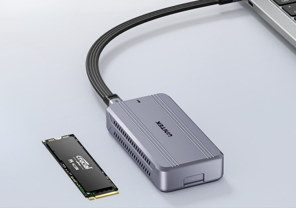 Obudowa dysku UNITEK S1242AGY01-EU Srebrna obudowa dysku z podłączonym czarnym kablem USB-C spoczywa na jasnym blacie, a obok niej leży pionowo czarny moduł pamięci M.2