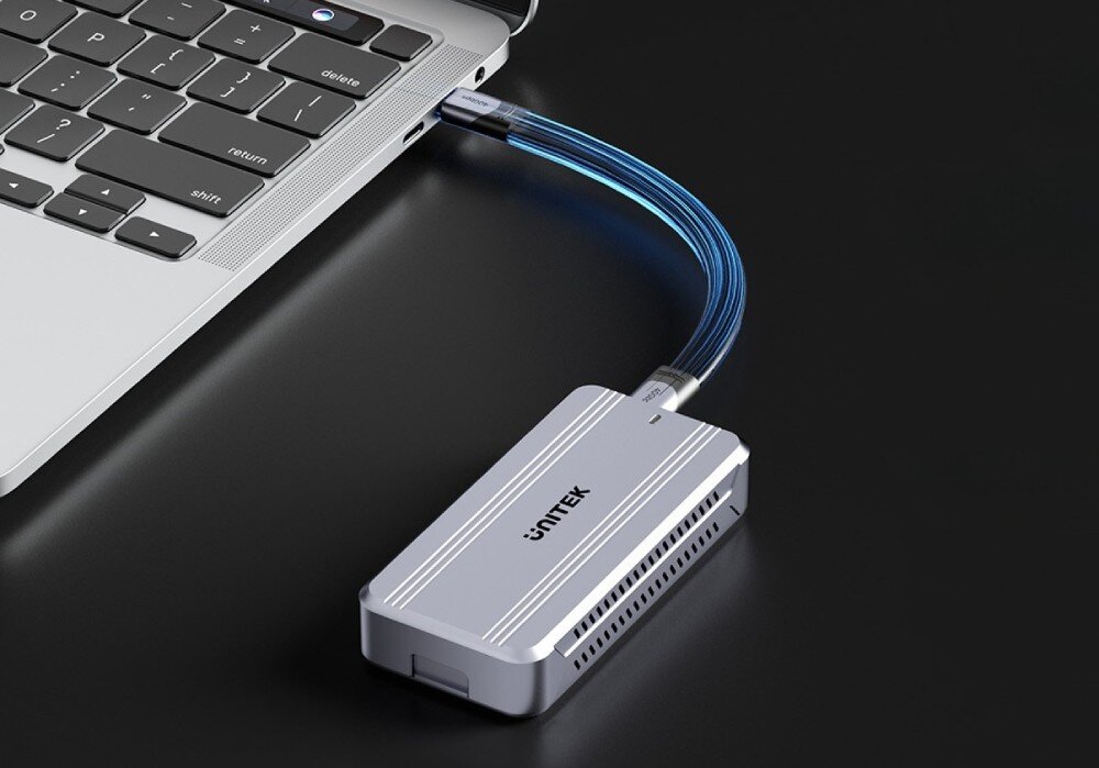 Obudowa dysku UNITEK S1242AGY01-EU Zbliżenie na bok srebrnego laptopa z podłączonym kablem USB-C, który jest podświetlony na niebiesko i prowadzi do srebrnej, żebrowanej obudowy dysku na czarnej powierzchni