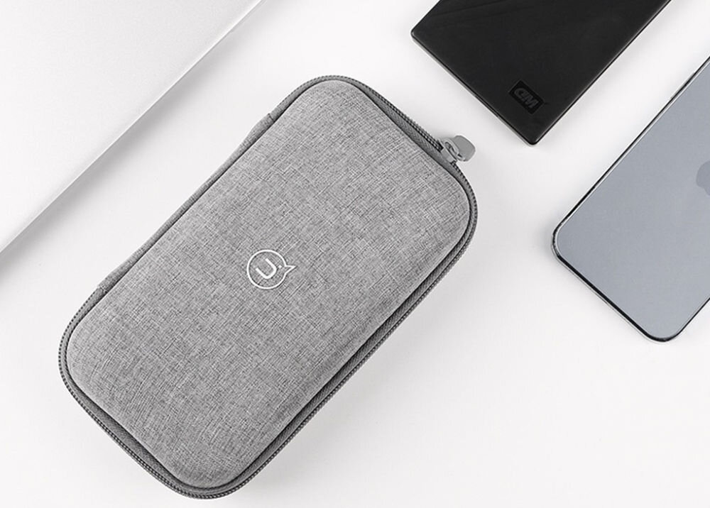Szare etui ochronne z zamkiem błyskawicznym, z widocznym logo producenta. Obok znajdują się czarne i srebrne urządzenia elektroniczne.