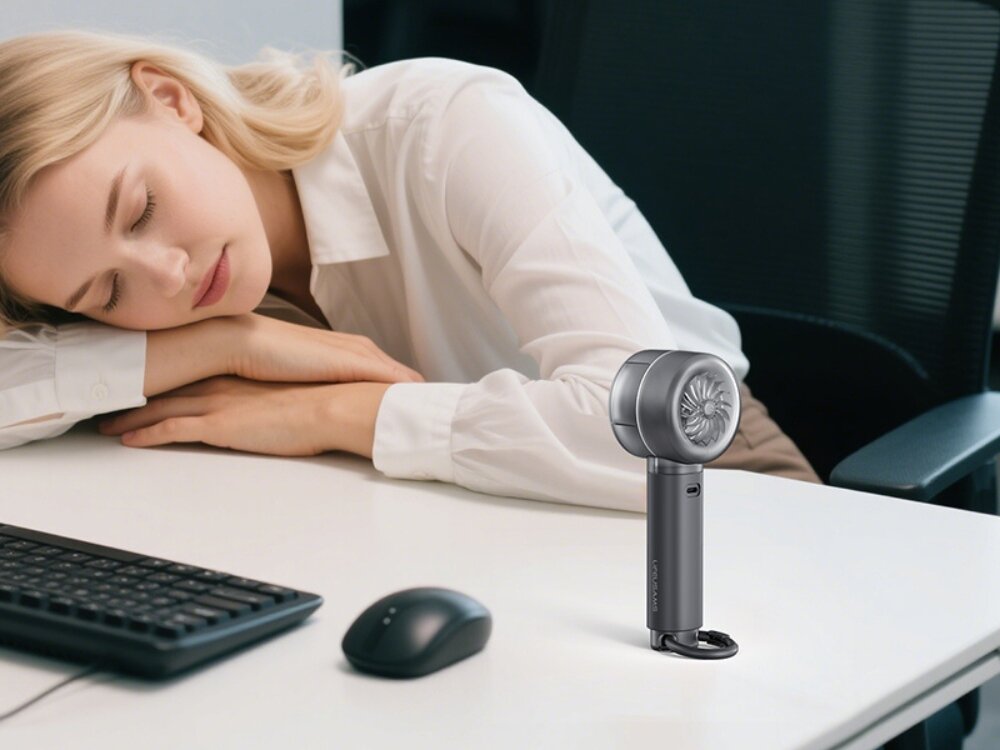 USAMS LU01 mini wentylator w podróży Szary wentylator przenośny postawiony na białym biurku obok klawiatury, przy którym drzemie pracownica biurowa.
