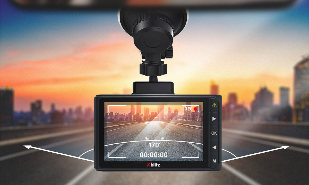 Obraz przedstawia wideorejestrator zamontowany na szybie samochodu, z widokiem na ekranie pokazującym drogę i budynki w tle. Na ekranie widoczny jest kąt 170°, czas 00:00:00 oraz logo \'xblitz\'.