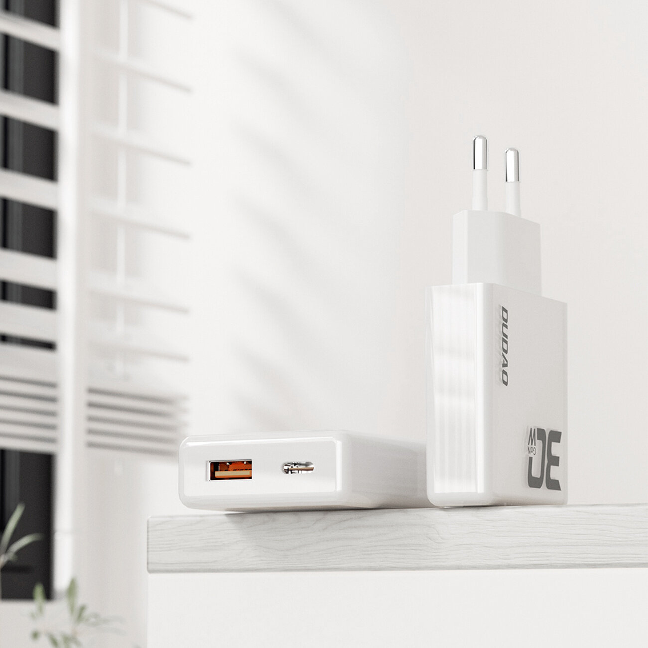 Na obrazie widoczna jest biała ładowarka sieciowa z dwoma wtykami oraz portami USB-A i USB-C. Na ładowarce znajduje się napis \'DUDAO\'.