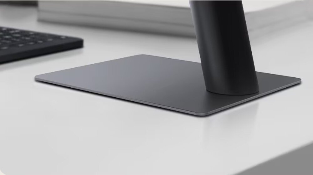 Monitor LG UltraWide 29U511A-B Zbliżenie na metalową podstawę monitora w kształcie prostokąta ustawioną na jasnym biurku z fragmentem klawiatury w tle