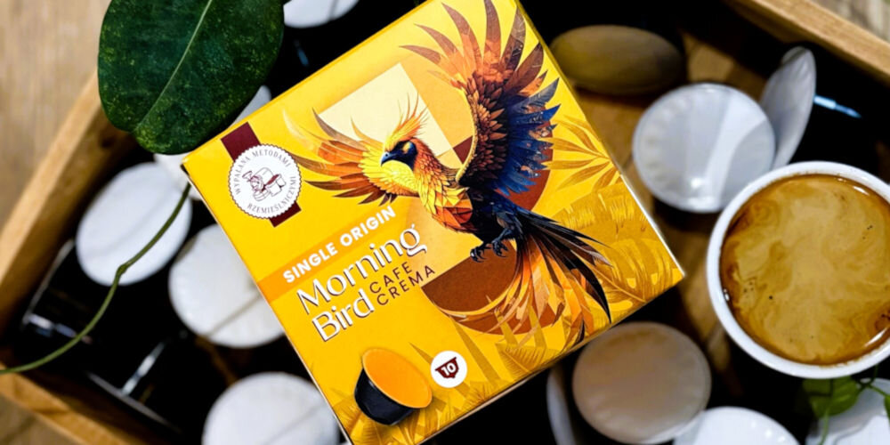Kapsułki MORNING BIRD Cafe Crema 10 szt. w żółtym opakowaniu z egzotycznym ptakiem na tle kapsułek i filiżanki z kawą
