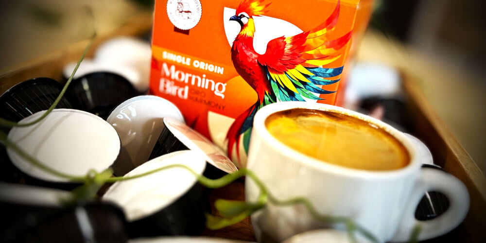 Kapsułki MORNING BIRD Oro Harmony 10 szt. w żółtym opakowaniu z egzotycznym ptakiem na tle kapsułek i filiżanki z kawą