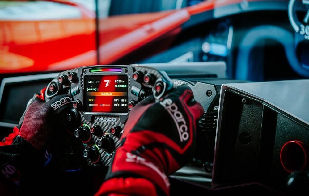 Baza kierownicy MOZA Racing R12 V2 RS081 na bazie założona kierownica na niej dłonie w tle ekran przedstawiający środek pojazdu algorytm Force Feedback szczegółowe informacje o zachowaniu auta zrozumienie fizyki jazdy możliwość odczytywania sygnałów