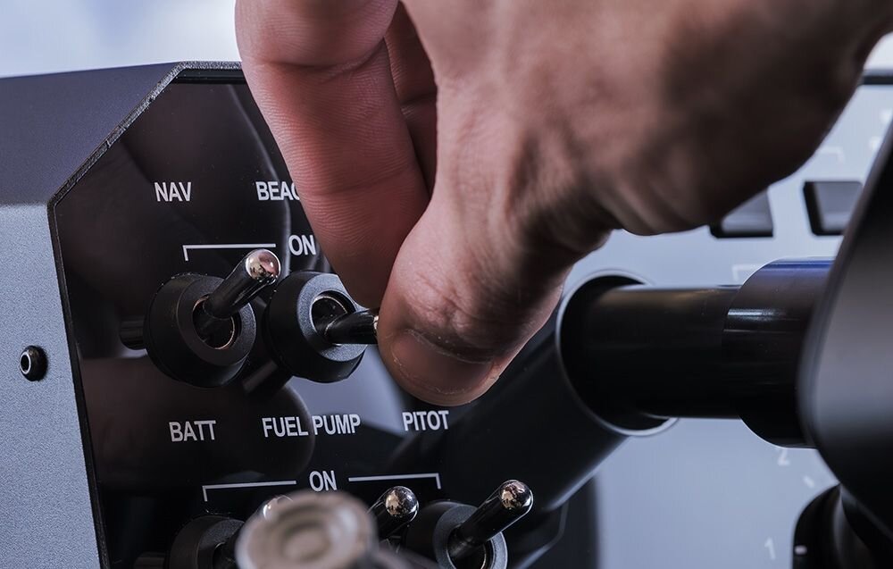 Baza na joystick yoke MOZA Racing AY210 (PC) Dłoń osoby obsługującej bazę z napisami NAV, BATT, FULET PUMP, PITOT i ON programowalne przełączniki, MOZA Cockpit, personalizacja, telemetria