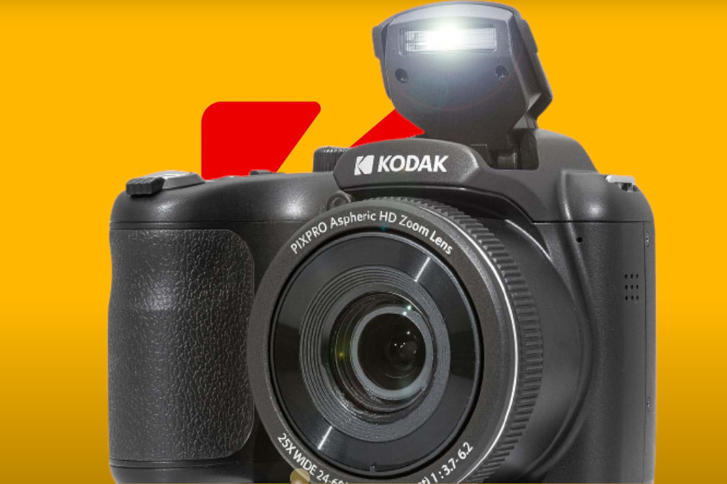 Czarny aparat fotograficzny marki KODAK z widocznym obiektywem i otwartą lampą błyskową. Na obiektywie napis \'PIXPRO Aspheric HD Zoom Lens\'.