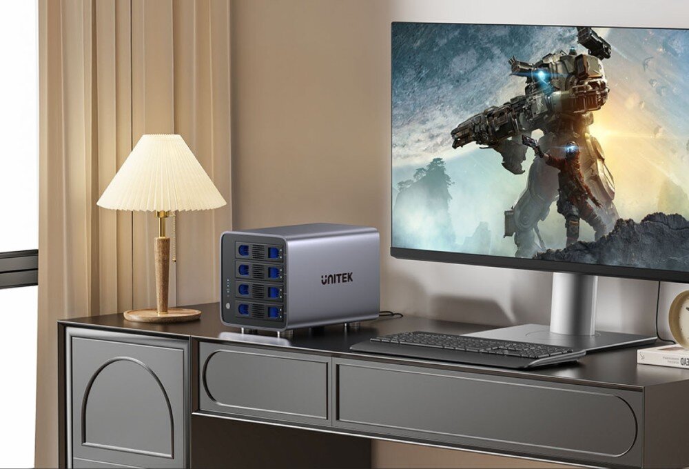 Obudowa dysku UNITEK S1301AGY01-EU Urządzenie do przechowywania danych stoi na biurku obok monitora wyświetlającego grafikę z robotem i lampy z jasnym kloszem. Całość znajduje się w nowocześnie urządzonym pokoju