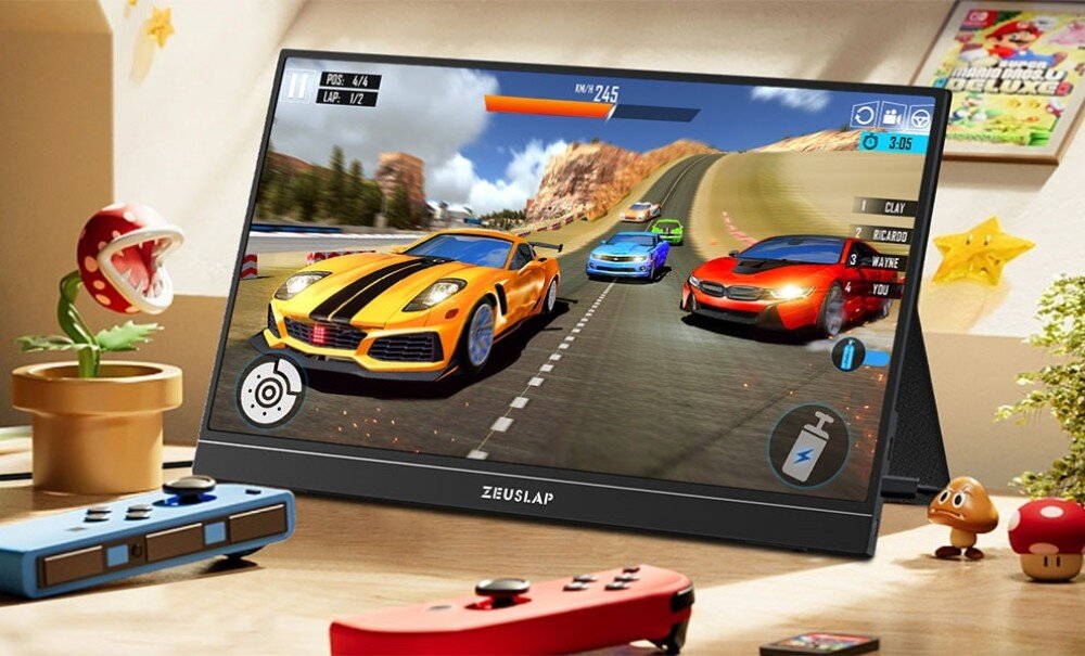 Monitor ZEUSLAP ZP156K Monitor na biurku wyświetlający grę wyścigową z żółtym samochodem sportowym na pierwszym planie, obok leży kontroler do konsoli, opis