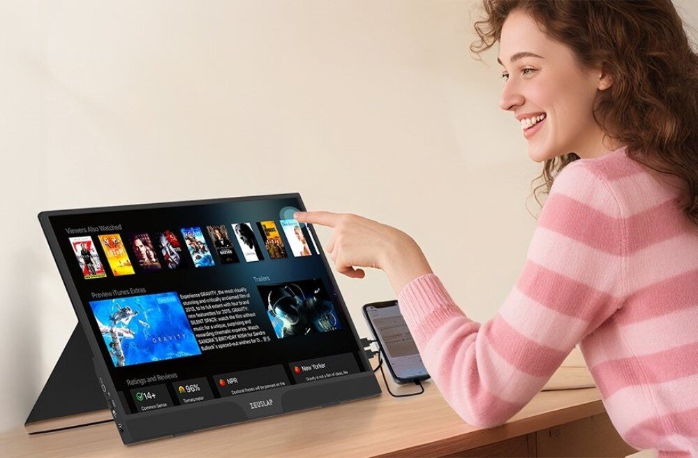 Monitor ZEUSLAP Z15ST Kobieta w różowym swetrze dotyka ekranu przenośnego monitora wyświetlającego bibliotekę filmów, przekątna, rozdzielczość, matryca, jakość obrazu